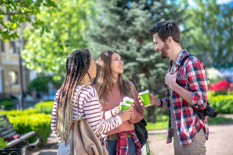 Tall guy and two long-haired girls with coffee in the square