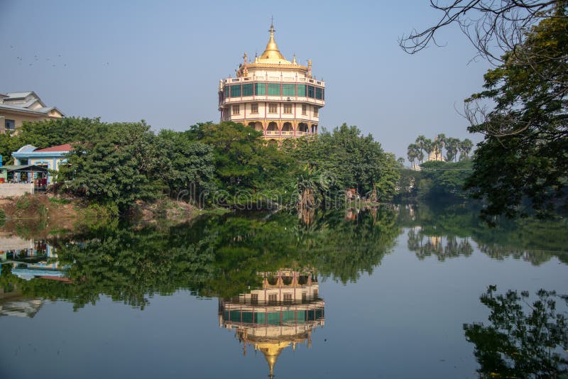 Tall octagonal tower, green tropical gardens, blue sky background and mirror image reflection in a still lake. Tranquil scene with monastery buildings and tower stock image Tall octagonal tower, green tropical gardens, blue sky background and mirror image reflection in a still lake. Tranquil scene with monastery buildings and tower stock image