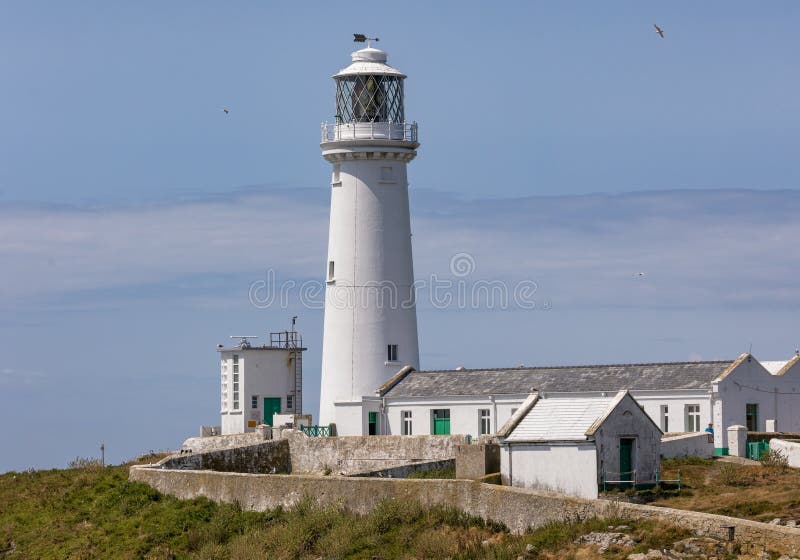 Tall white stone lighthouse at the edge of the cliffs on a rugged coastline. South Stack Lighthouse stock photography