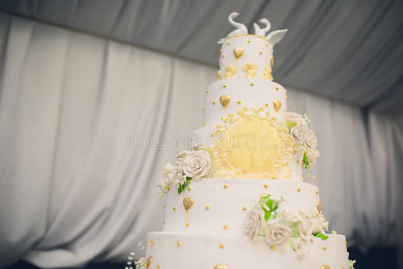 A tall white wedding cake decorated with gold flowers and white swans. Two pieces are cut off.