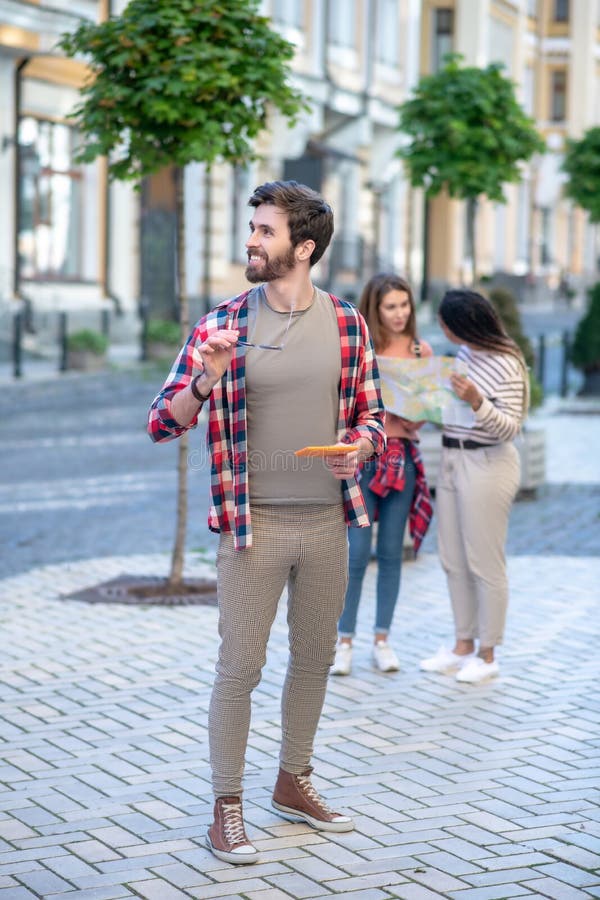 Tall young guy holding sunglasses and tablet outdoors