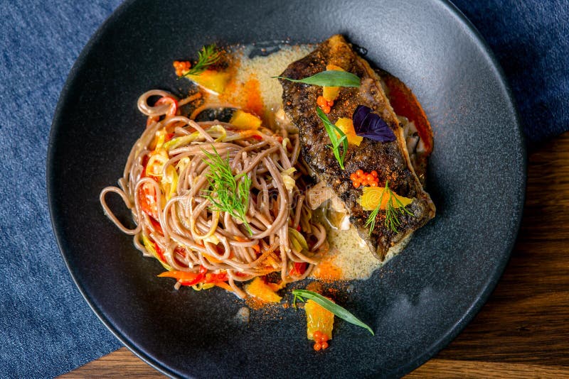 Tallarines del alforfón en el wok y la carpa cocida Cocina asiática El trabajo de un cocinero profesional Plato de un menú del re imagen de archivo libre de regalías Tallarines del alforfón en el wok y la carpa cocida Cocina asiática El trabajo de un cocinero profesional Plato de un menú del re imagen de archivo libre de regalías
