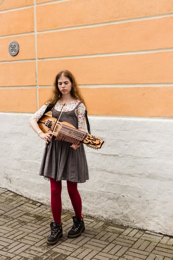 TALLIN, ESTÔNIA - CERCA DE 2016: Um músico da rua da fêmea joga o nyckelharpa em uma caminhada lateral na cidade velha de Tallin foto de stock TALLIN, ESTÔNIA - CERCA DE 2016: Um músico da rua da fêmea joga o nyckelharpa em uma caminhada lateral na cidade velha de Tallin foto de stock