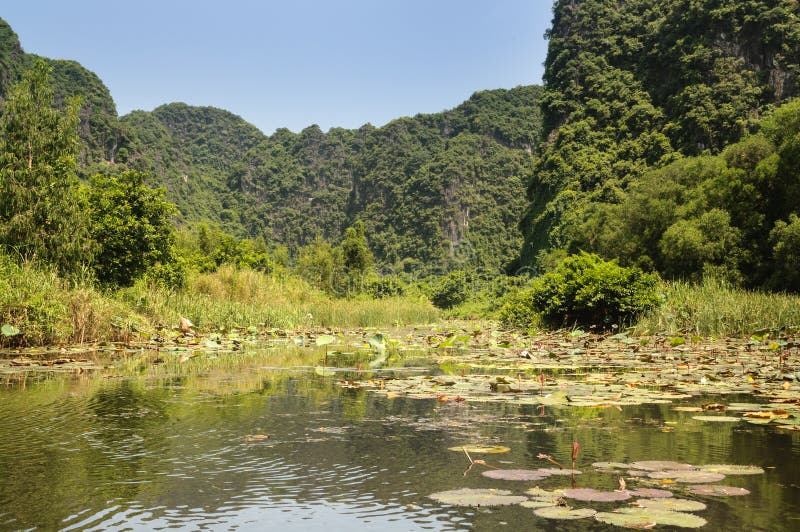 Tam coc, Vietnam; 08 10 2019: Sampan boat-ride, rowed by a villager at Tam Coc , Vietnam : the karst landscape with many vertical sides and covered by much green vegetation. Tam coc, Vietnam; 08 10 2019: Sampan boat-ride, rowed by a villager at Tam Coc , Vietnam : the karst landscape with many vertical sides and covered by much green vegetation.