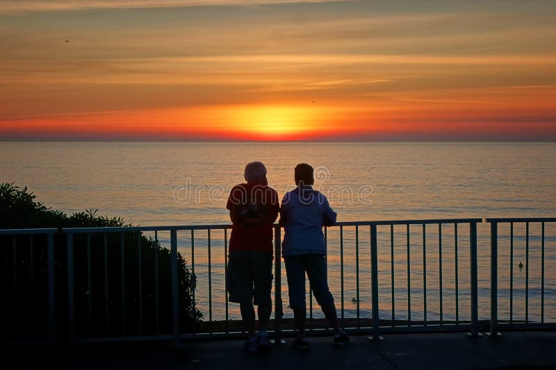 A couple hangs out at the railing watching the sun set..