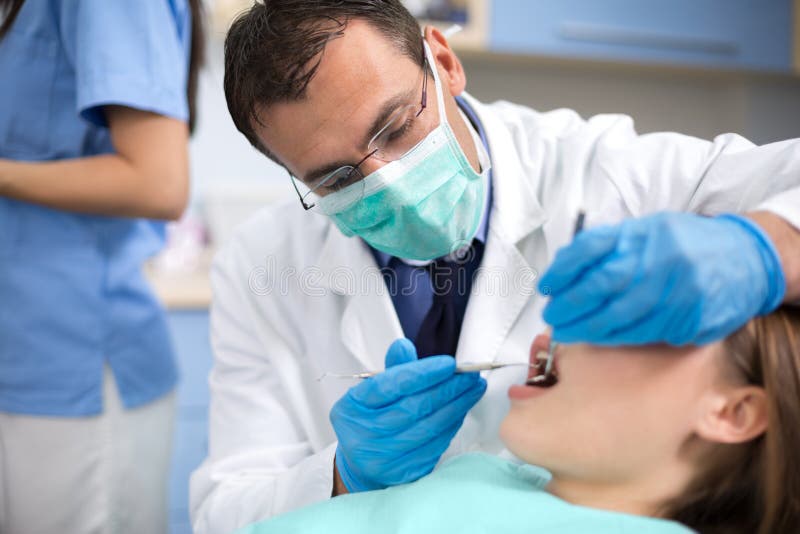 Tandarts met beschermende masker en van de handschoenenreparatie tand van zijn clie stock foto's Tandarts met beschermende masker en van de handschoenenreparatie tand van zijn clie stock foto's