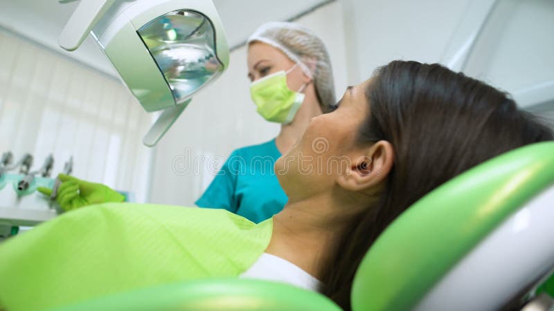 Tandläkare som behandlar tanden till den unga kvinnan, kariesborttagning, tand- tätningsmedelplacering