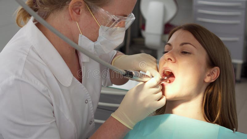 Tandläkare som behandlar tänder till kvinnapatienten i klinik Kvinnlig yrkesmässig doktor på arbete tand- checkup