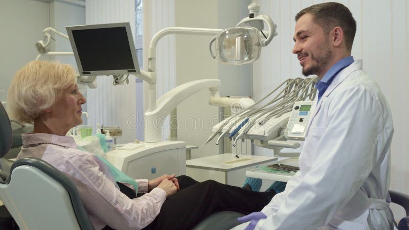 Tandläkaren hälsar den kvinnliga klienten på hans kontor