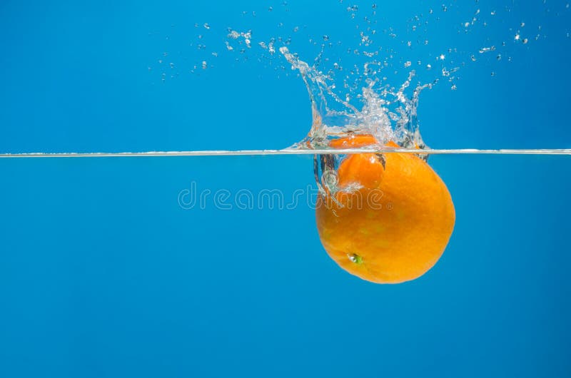 Tangerine in Water with Splashes on a Blue Background Stock Image