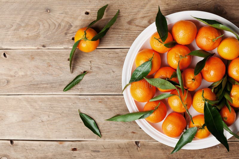 Tangerines or mandarins with green leaves on vintage wooden table from above in flat lay style.