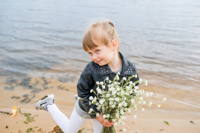 Tanzendes kaukasisches Mädchen in der Jacke, halten Wildflowers neben einem See in einem Park stockbild Tanzendes kaukasisches Mädchen in der Jacke, halten Wildflowers neben einem See in einem Park stockbild