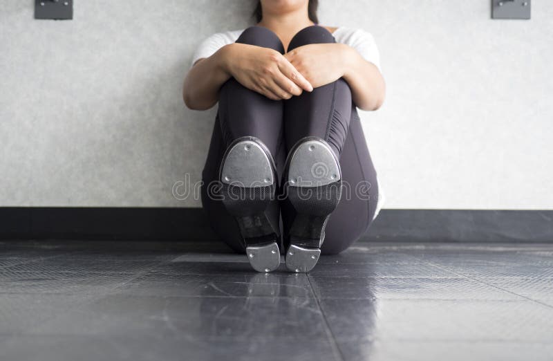 Tapdanserzitting die neer, kranen tonen, en haar benen houden stock afbeelding Tapdanserzitting die neer, kranen tonen, en haar benen houden stock afbeelding