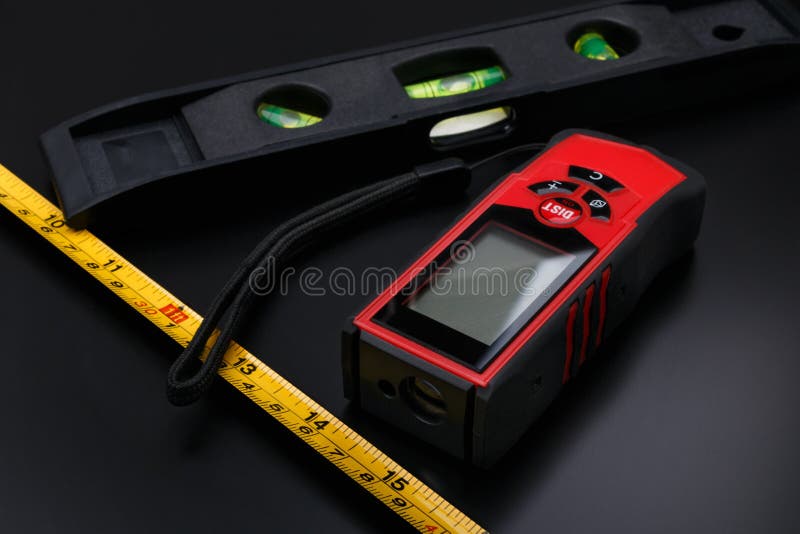 Tape measure, red laser tape and short building level on black matte surface