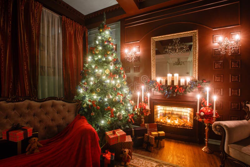 Tarde de la Navidad por luz de una vela apartamentos clásicos con una chimenea blanca, un árbol adornado, sofá, ventanas grandes