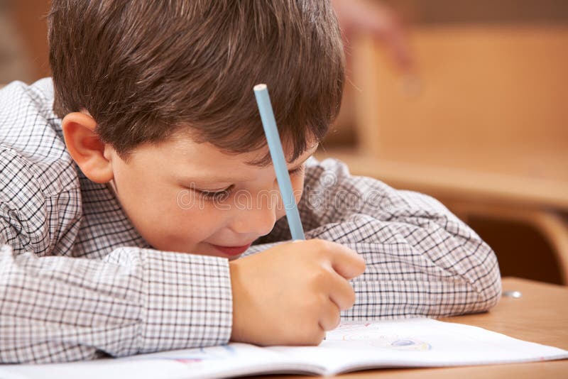 Photo of clever schoolkid writing something in his copybook at lesson. Photo of clever schoolkid writing something in his copybook at lesson