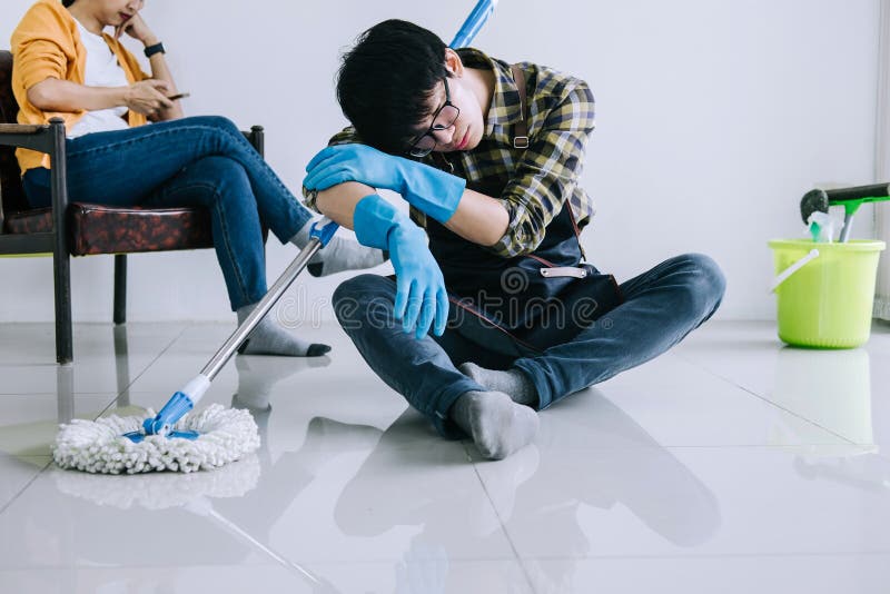 Tarefas domésticas do marido e conceito da limpeza, homem cansado nas luvas de borracha azuis que limpam a poeira usando o espana imagens de stock Tarefas domésticas do marido e conceito da limpeza, homem cansado nas luvas de borracha azuis que limpam a poeira usando o espana imagens de stock