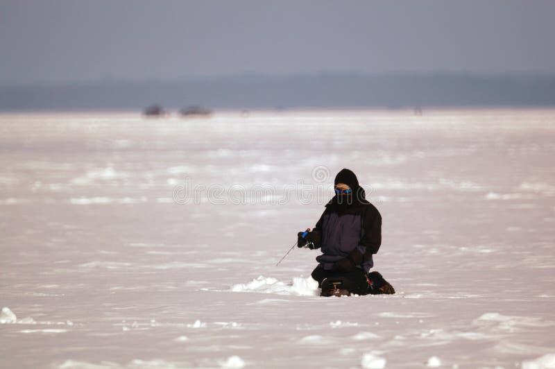 A man sits patiently while ice fishing on a cold winter day. A man sits patiently while ice fishing on a cold winter day.