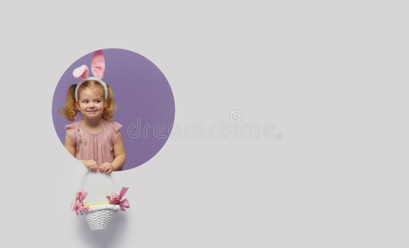 Easter card. Cute little child girl with bunny ears holding basket of Easter eggs. Child in a round hole circle in colored purple and white background. Mockup and copy space for text. Easter card. Cute little child girl with bunny ears holding basket of Easter eggs. Child in a round hole circle in colored purple and white background. Mockup and copy space for text