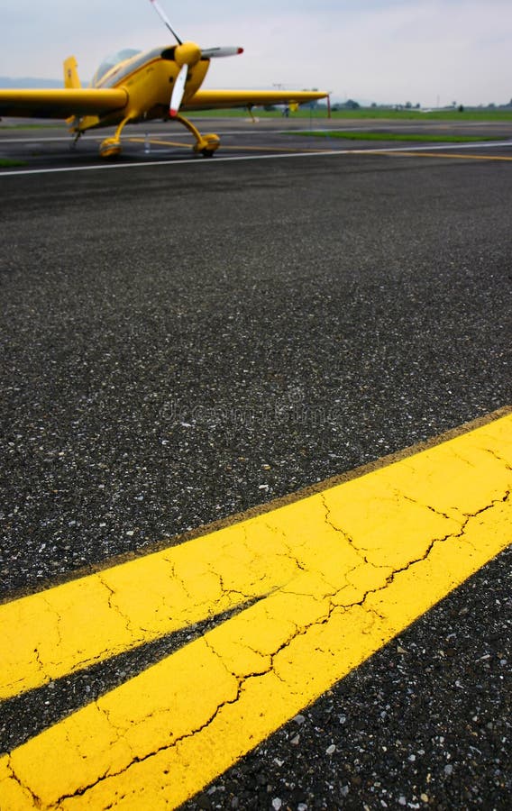 Yellow lines on the tarmac with aerobatics plane in background