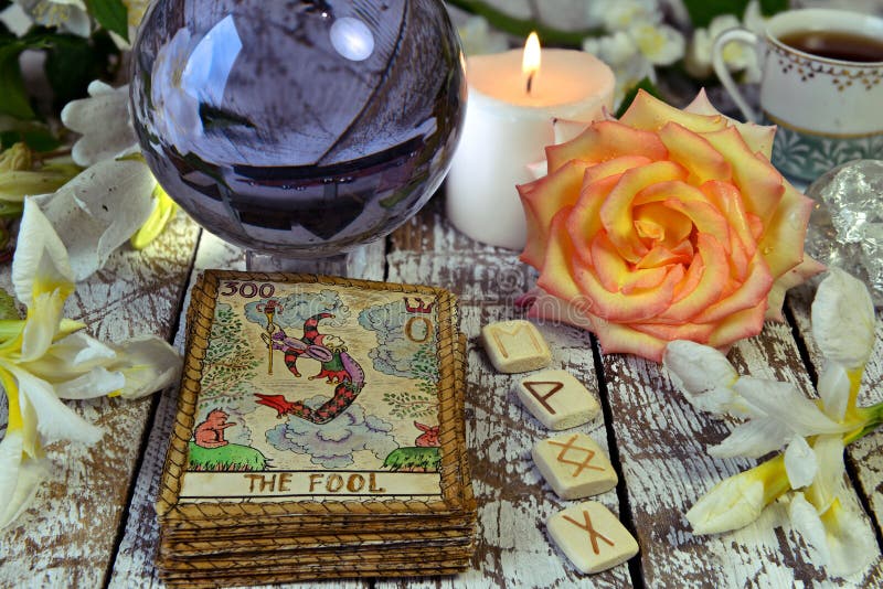 Tarot cards deck, crystal ball, runes and flowers on witch table
