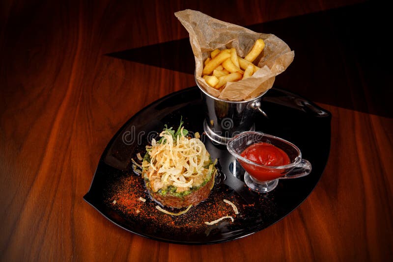 Tartar de carne cruda con cebollas patatas fritas y salsa en un plato oscuro fotos de archivo libres de regalías