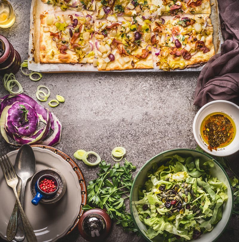 Tarte flambee or open vegetable pie with vegetables and green salad on rustic kitchen table background with plates, cutlery and to