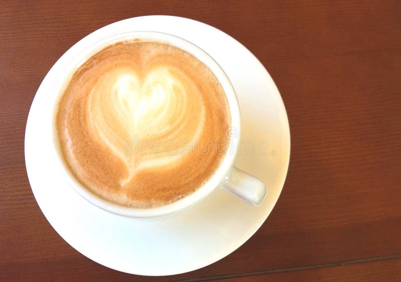 Tasse blanche avec du café italien de cappuccino avec le modèle sous forme de belle fin de coeur sur le fond en bois photographie stock libre de droits Tasse blanche avec du café italien de cappuccino avec le modèle sous forme de belle fin de coeur sur le fond en bois photographie stock libre de droits