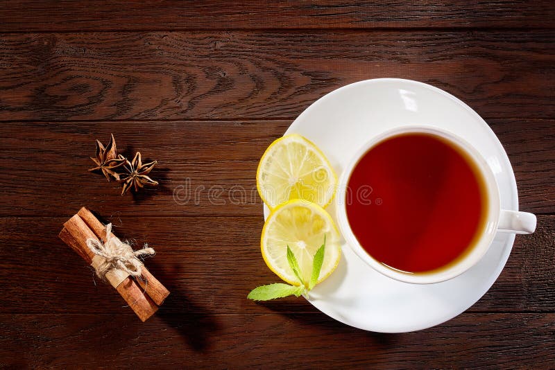 Tasse blanche de thé avec les bâtons de cannelle, le citron, les feuilles en bon état et le tamis de thé sur la table rustique en photographie stock libre de droits Tasse blanche de thé avec les bâtons de cannelle, le citron, les feuilles en bon état et le tamis de thé sur la table rustique en photographie stock libre de droits
