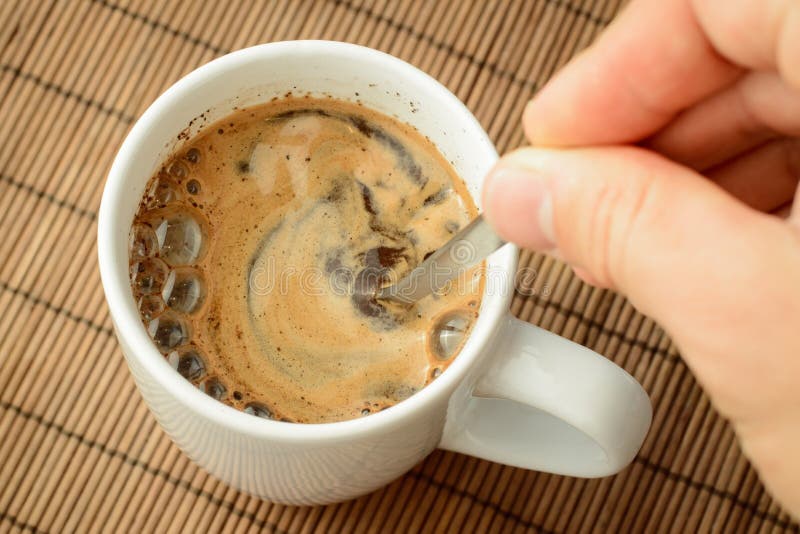 Tasse de café aromatique noir sur fond brun. Mans brasse le café à la main avec beaucoup de mousse avec une cuillère. faire du café le matin
