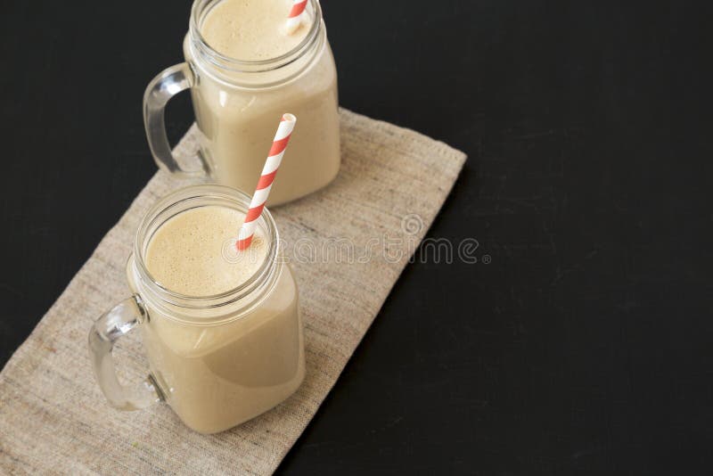 Tasses en verre de pot de maçon remplies de smoothie de banane de beurre d'arachide sur une surface noire, vue d'angle faible Cop photographie stock libre de droits Tasses en verre de pot de maçon remplies de smoothie de banane de beurre d'arachide sur une surface noire, vue d'angle faible Cop photographie stock libre de droits