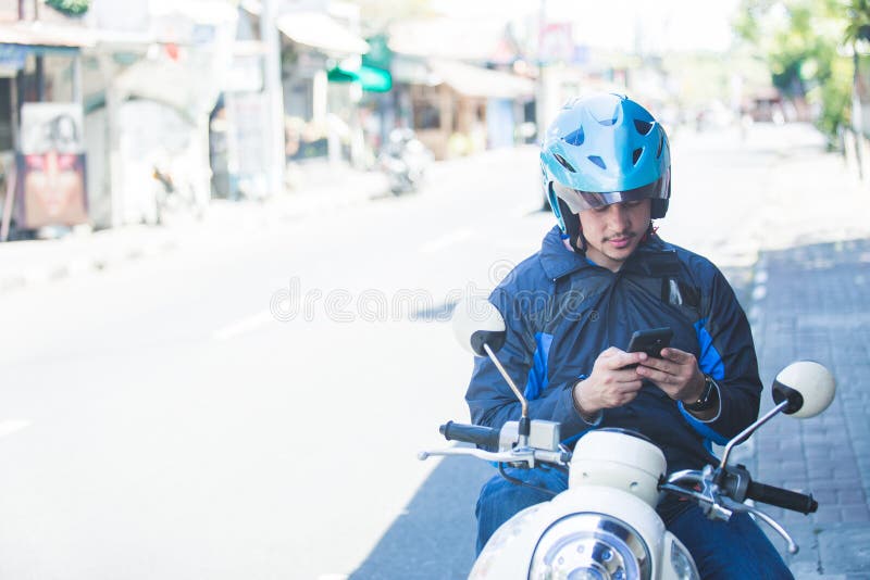 Tassista del motociclo che manda un sms sul cellulare dal lato del fotografia stock libera da diritti Tassista del motociclo che manda un sms sul cellulare dal lato del fotografia stock libera da diritti