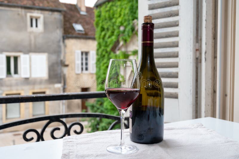 Tasting of burgundy red wine from grand cru pinot noir  vineyards, glass and bottle of wine and view on old town street in
