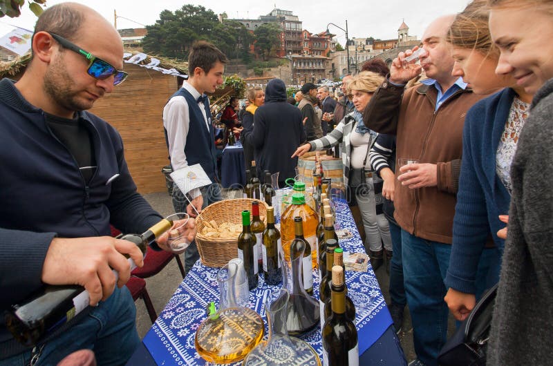 Tasting lass with crowd of people drinking wine with bartender at festival of Georgia