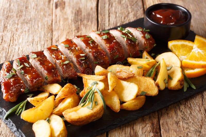 Tasty baked pork tenderloin in honey-orange glaze with potato wedges close-up on a plate. horizontal