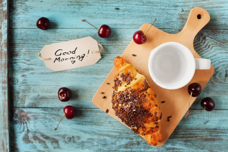 Tasty breakfast with fresh croissant, empty cup of coffee, cherries and notes on a wooden table stock image Tasty breakfast with fresh croissant, empty cup of coffee, cherries and notes on a wooden table stock image