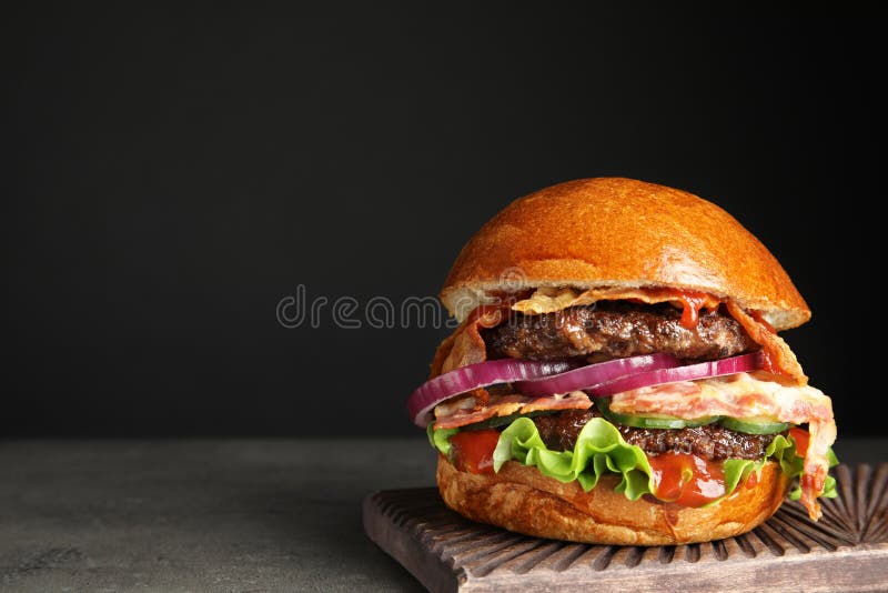 Tasty burger with bacon on table against black. Space for text