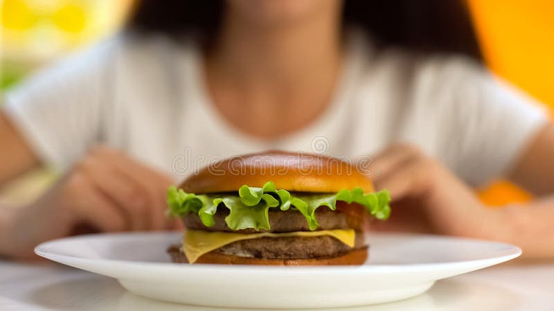Tasty burger lying on plate, female on background, fast food restaurant, meal royalty free stock photo Tasty burger lying on plate, female on background, fast food restaurant, meal royalty free stock photo