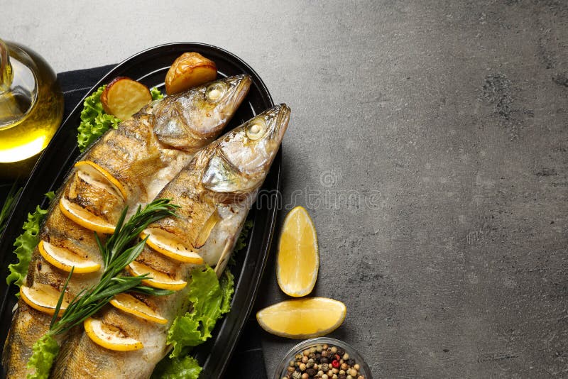 Tasty homemade roasted pike perches served on grey table, flat lay and space for text. River fish stock photography