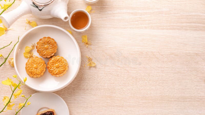 Tasty moon cake for Mid-Autumn festival on bright wooden table, concept of festive afternoon tea decorated with yellow flowers