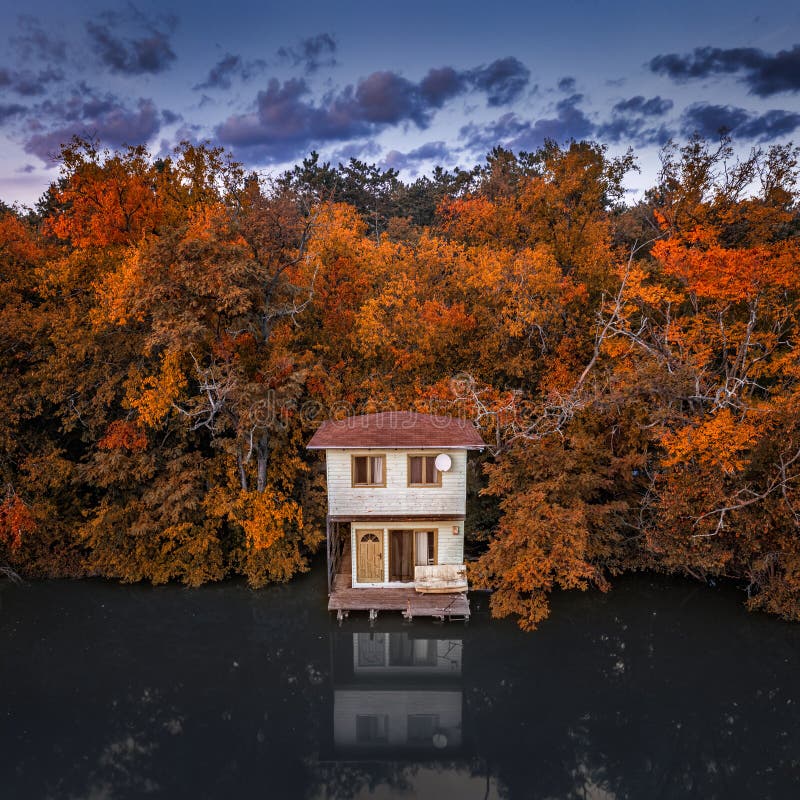Tata, Hungary - Aerial view of a romantic fisherman`s cabin by the Lake Derito with blue sky and autumn foliage