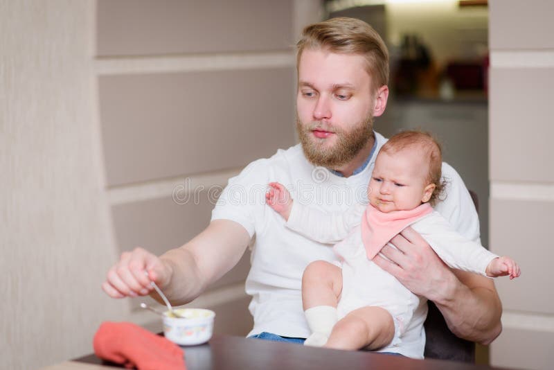 Tata karmi swoje niegrzeczne dziecko, które odmawia jedzenia puree owocowego. Ojciec karmi swoje kapryśne dziecko, które odmawia jedzenia puree owocowego