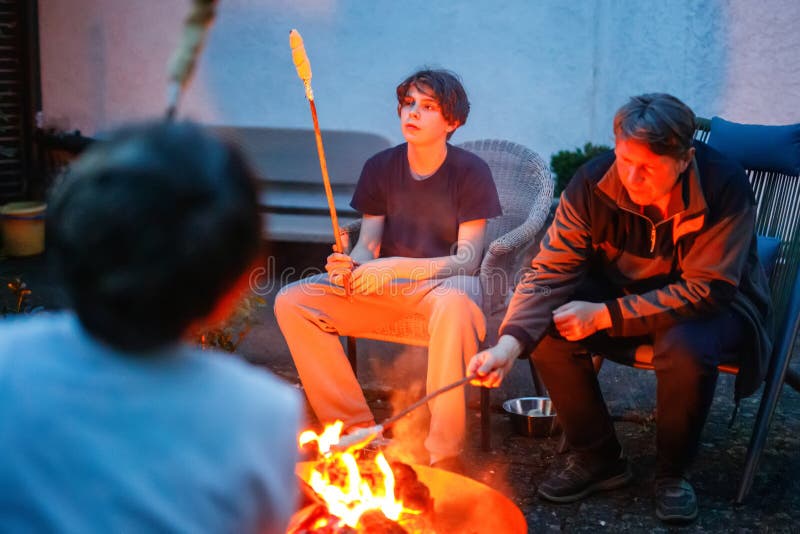 Tata și doi adolescenți stând lângă foc de tabără și coacând turtă. Familie împreună. Legătura dintre tată și copii stock photos