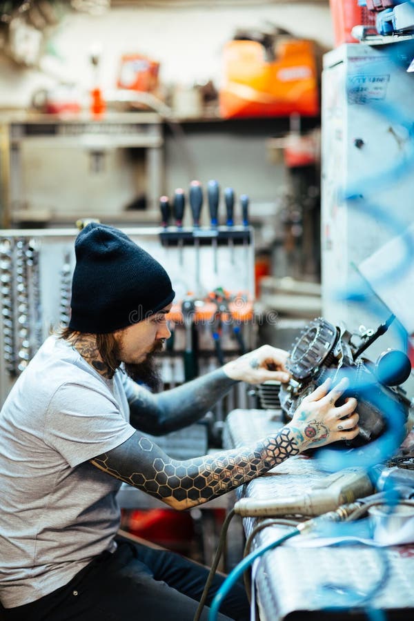 Tattooed Mechanic Checking Engine Part royalty free stock photos