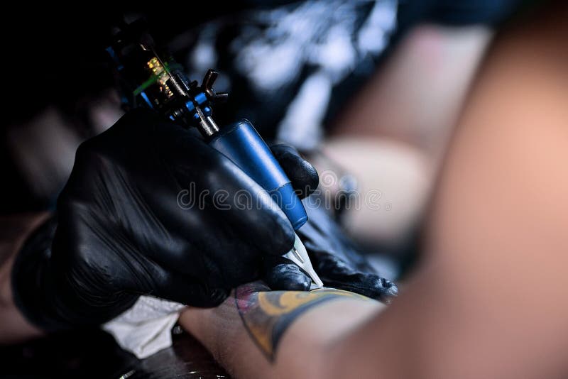 Tatueringkonstnär som gör tatueringen Förlagearbeten på den yrkesmässiga maskinen och i sterila svarta handskar royaltyfri fotografi Tatueringkonstnär som gör tatueringen Förlagearbeten på den yrkesmässiga maskinen och i sterila svarta handskar royaltyfri fotografi