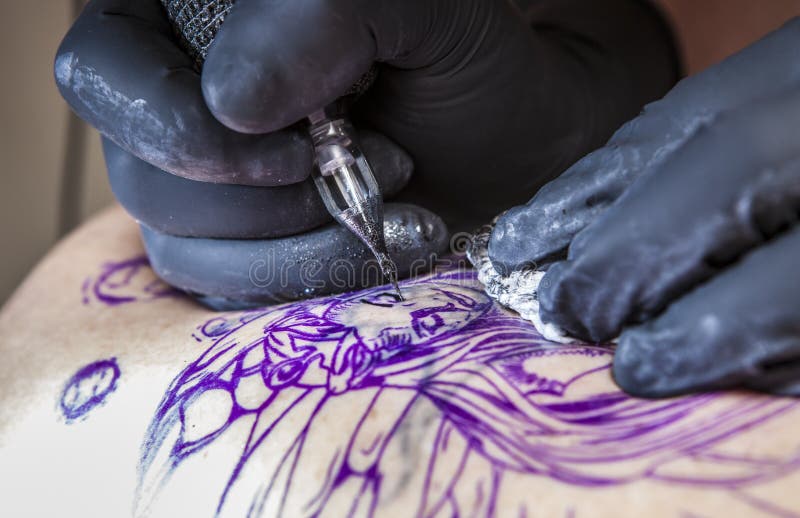 Tatueringkonstnären applicerar tatueringen till skulderbladen av en kvinna royaltyfria foton Tatueringkonstnären applicerar tatueringen till skulderbladen av en kvinna royaltyfria foton