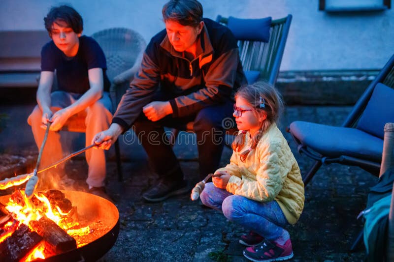 Tată fetiță școală și adolescent băiat stau de tabără foc și copt stickbread. Familie împreună. Legătura dintre tată și copii royalty free stock image