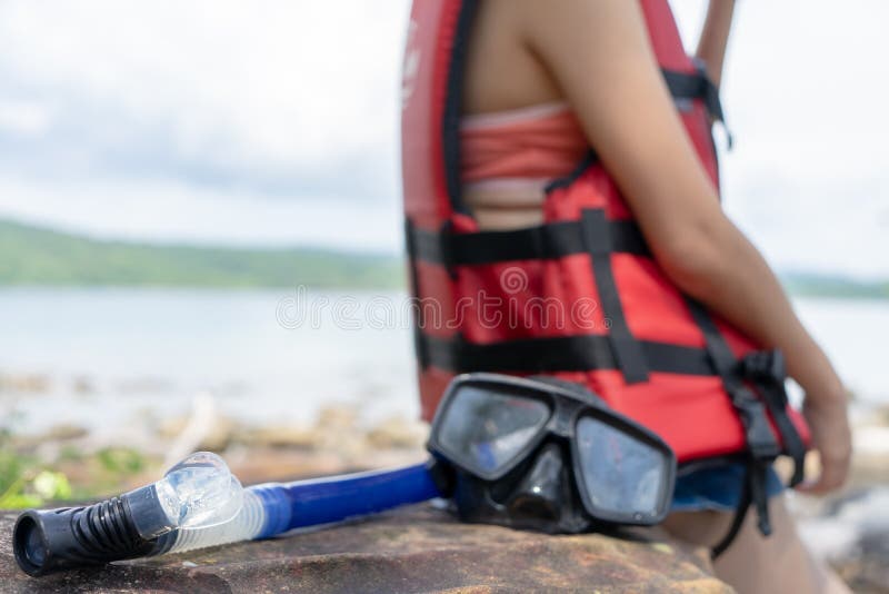 Tauchender Maske und Schnorchel-Gang auf Strandstein mit der tragenden Schwimmweste der Frau, die an den Sommerferien sich entspa lizenzfreie stockbilder Tauchender Maske und Schnorchel-Gang auf Strandstein mit der tragenden Schwimmweste der Frau, die an den Sommerferien sich entspa lizenzfreie stockbilder