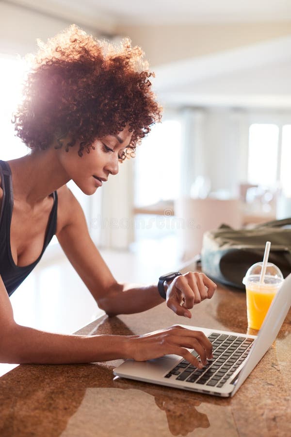 Tausendjährige Afroamerikanerfrau, die Eignung App auf Uhr und Laptop nach Training, Vertikale überprüft stockbild