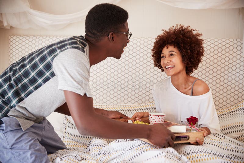 Tausendjährige Afroamerikanerpaare, die, Mann oben dient sein Partnerfrühstück im Bett, Abschluss feiern stockfoto